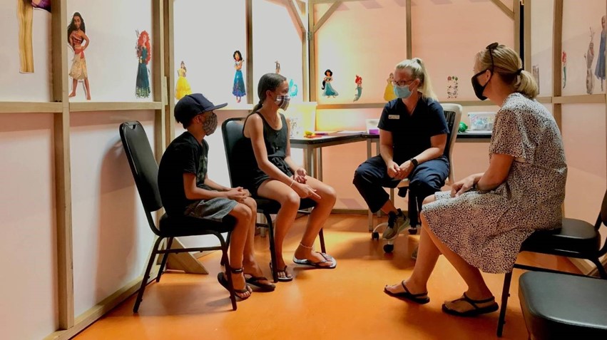 Two children sit with two doctors discussing the COVID vaccinations